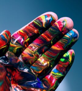 Main peinte d'un mélange de couleurs vives qui se fondent entre elles, symbole d'inclusion et de diversité.